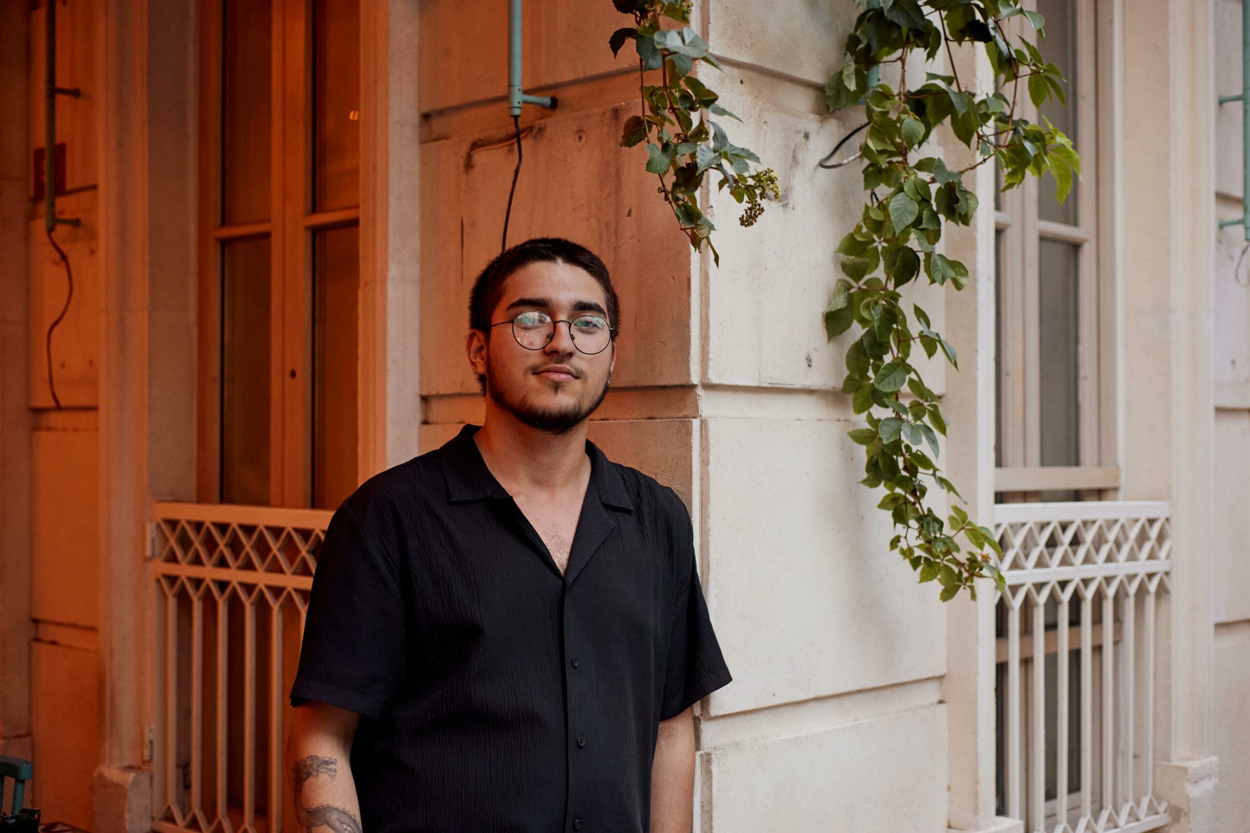 A man in glasses stands beside a building adorned with greenery in Istanbul.